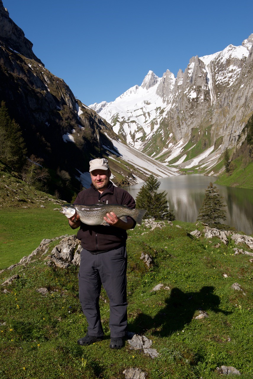 Mann hält Fisch in der hand vor imposanter Bergkulisse